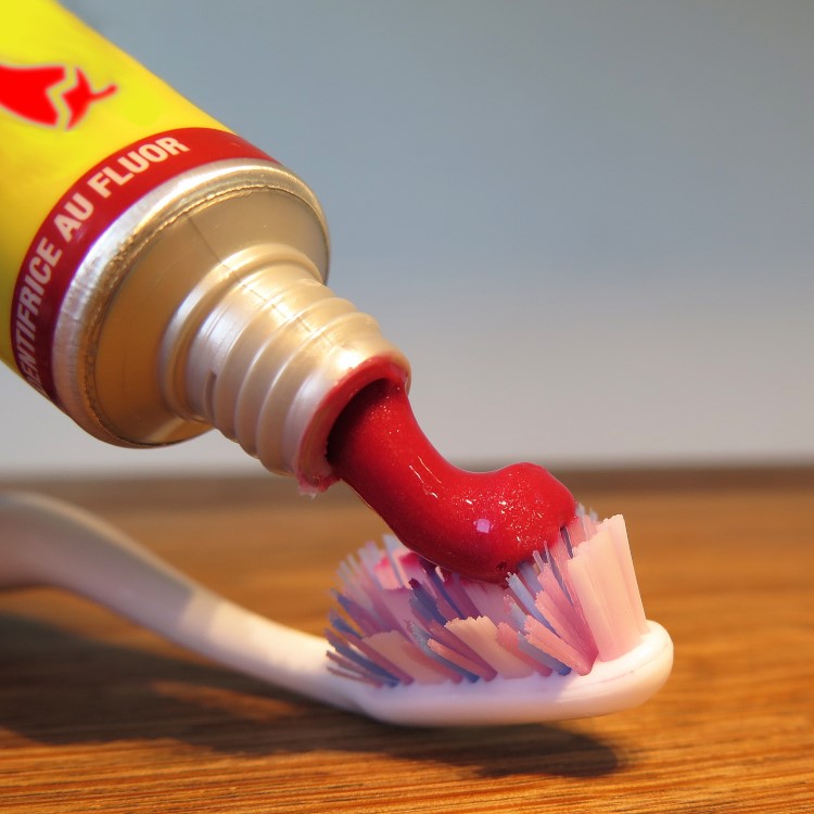 closeup of red toothpaste being squeezed onto a brush